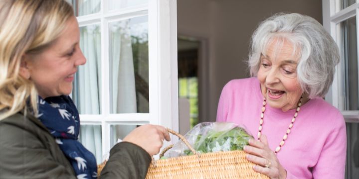 A woman delivering a basket of shopping to an elderly lady