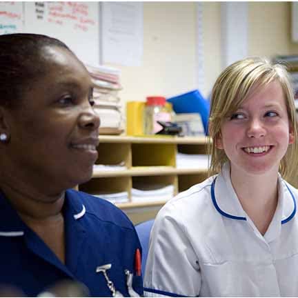 Photograph of two nurses or midwives sitting in a clinical room.