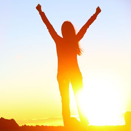 Photo of a woman facing the sun, raising her arms in celebration or joy.